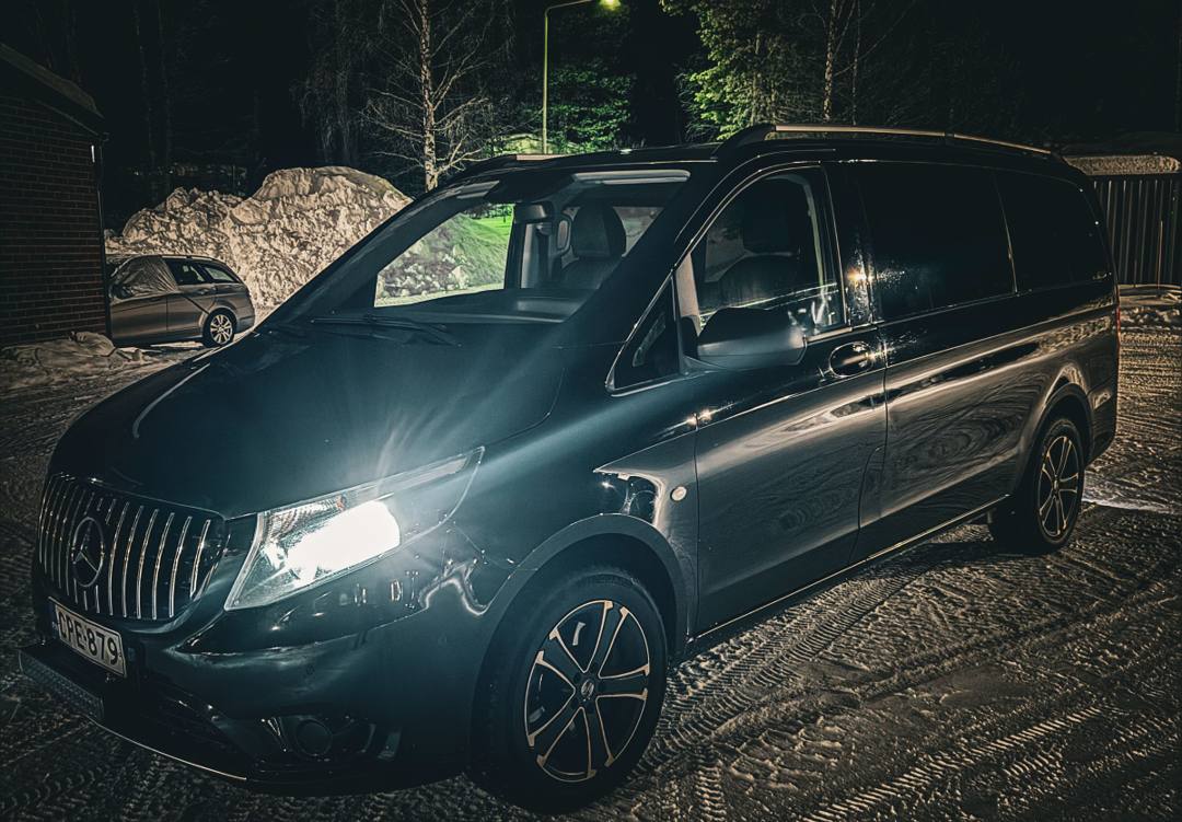 Black Mercedes-Benz van with headlights on in a snowy yard at night